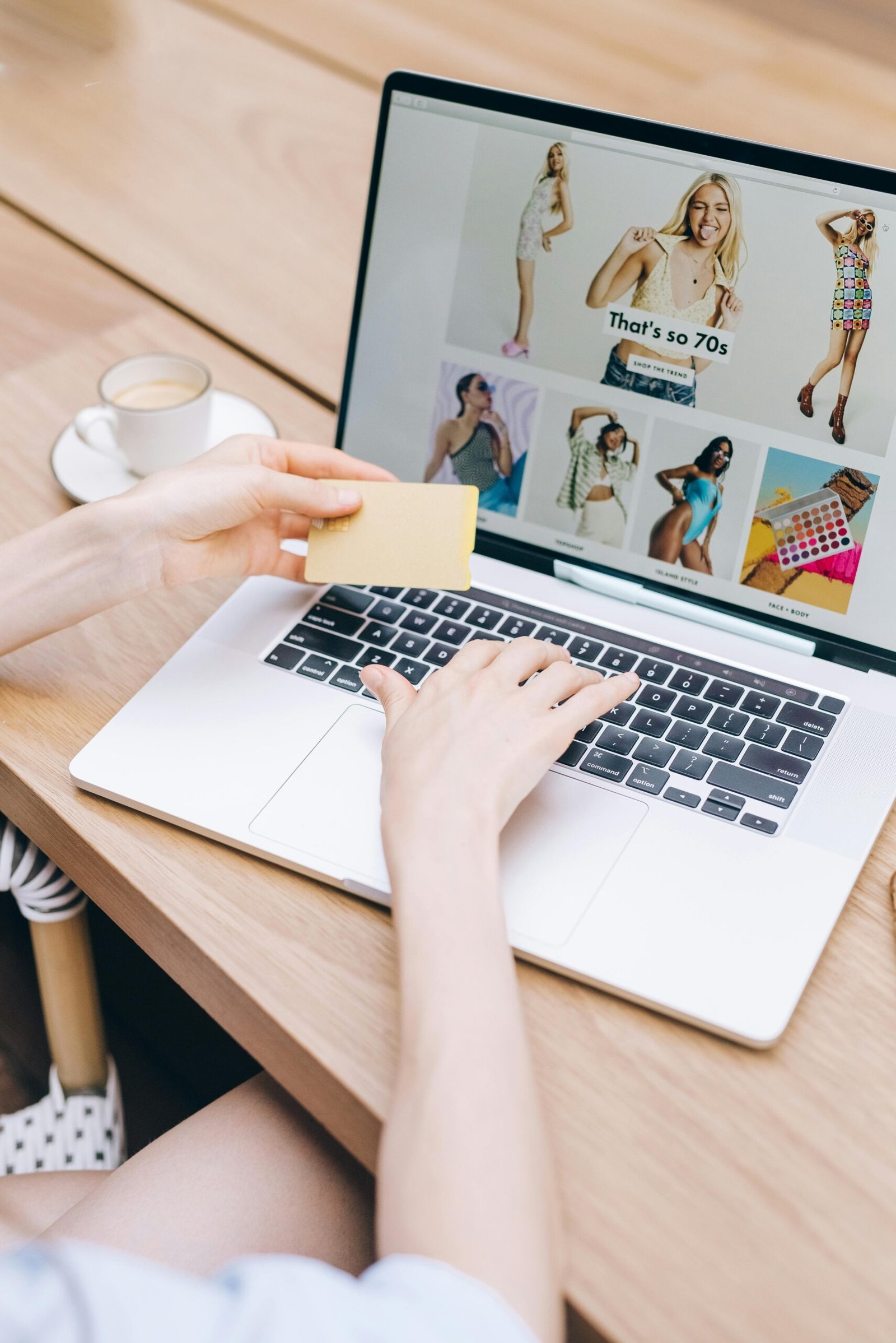 Hands holding a credit card while online shopping on a laptop at a wooden table.